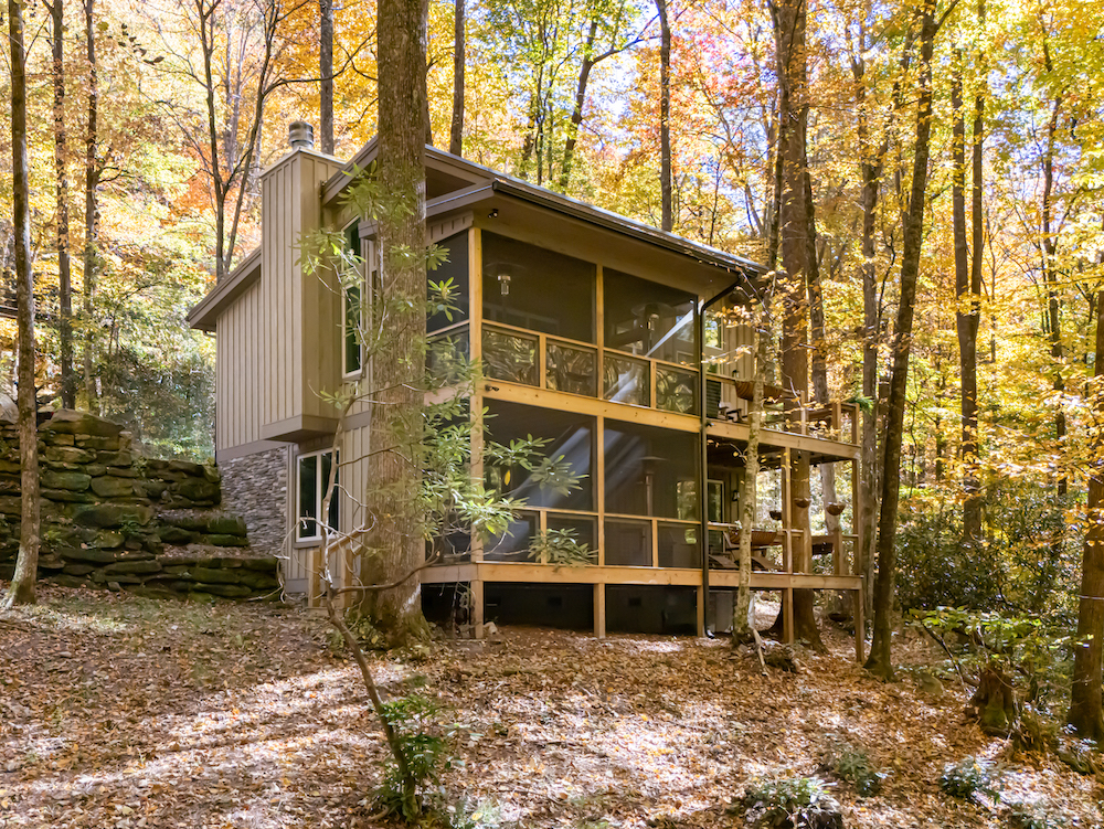 Custom mountain home by Powell Construction set into sloped Western North Carolina terrain, with dry-stack stone retaining wall and elevated foundation visible