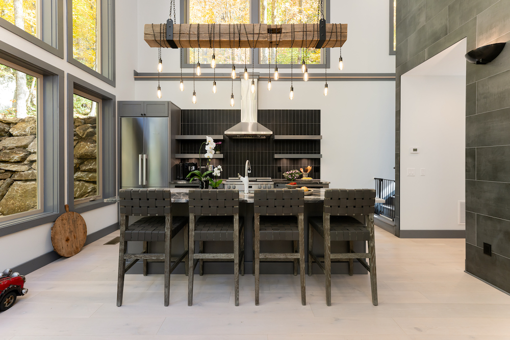 Custom mountain kitchen by Powell Construction showing reclaimed timber beam light fixture with custom metal strapping, full-height tile, integrated appliances, and high-craft millwork — the kind of detail that separates accurate estimates from low bids
